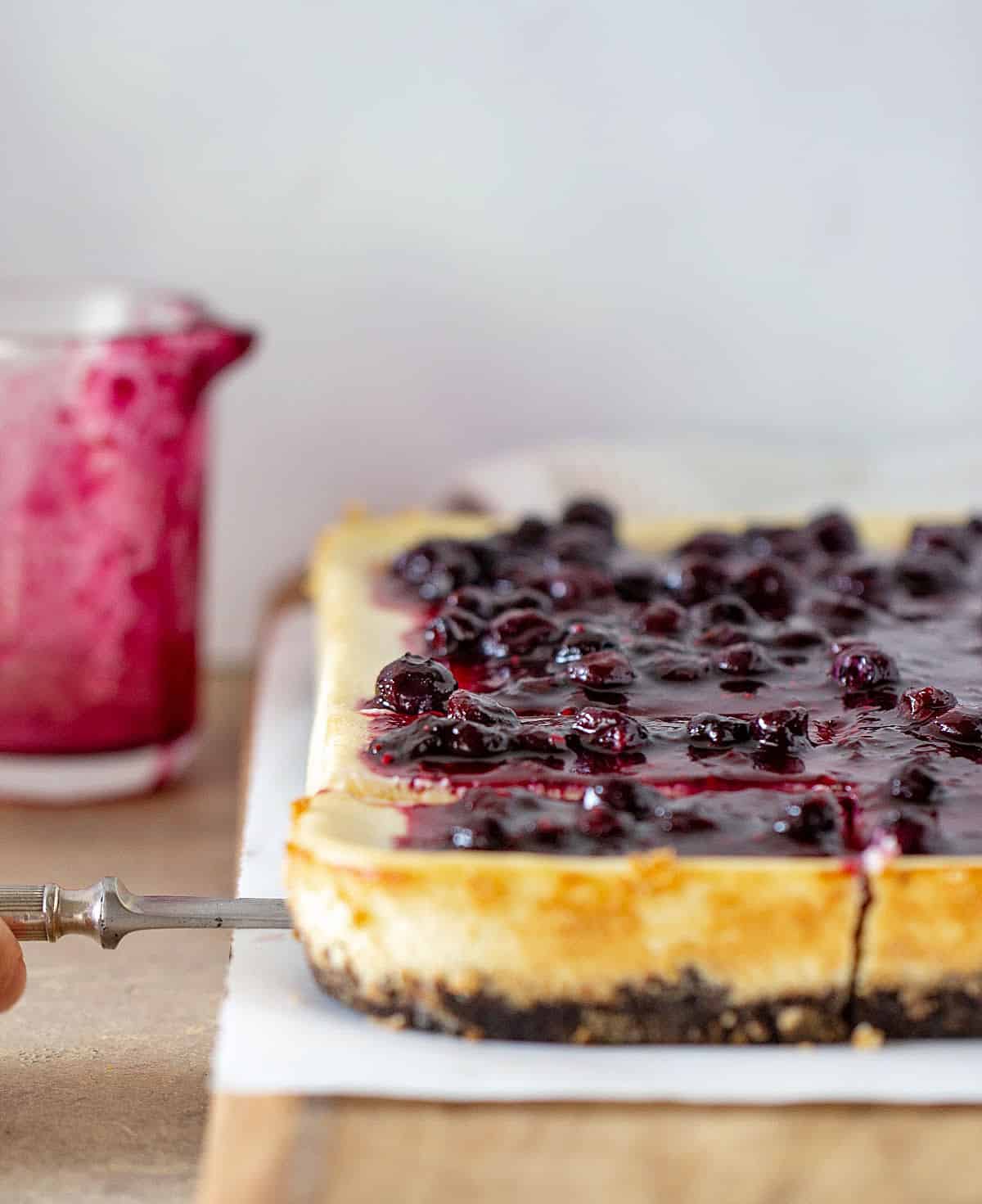 Berry topped cheesecake on wooden board, sauce jar