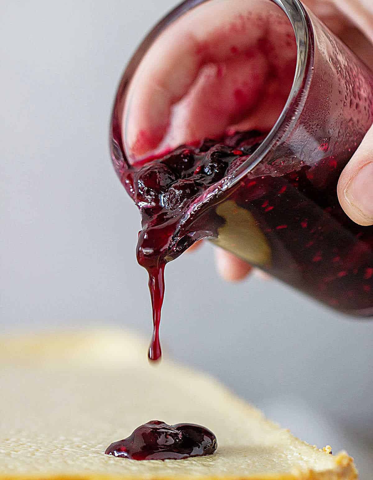 Jar pouring berry sauce on cheesecake