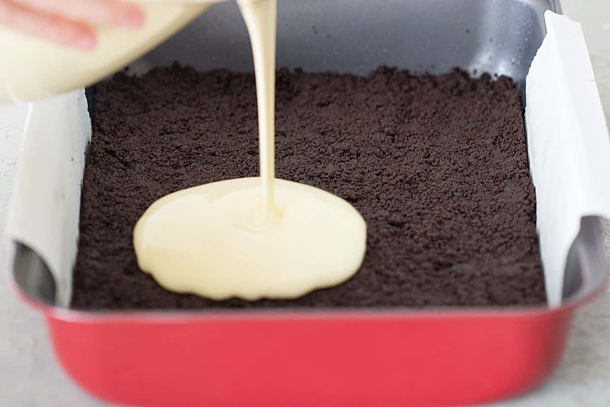 Chocolate cheesecake base on red pan; cheesecake filling being poured
