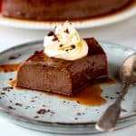 Grey plate with single serving of chocolate flan with dollop of cream and a silver spoon