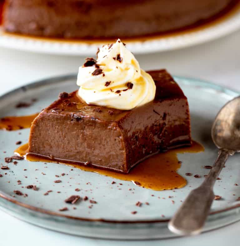 Grey plate with single serving of chocolate flan with dollop of cream and a silver spoon