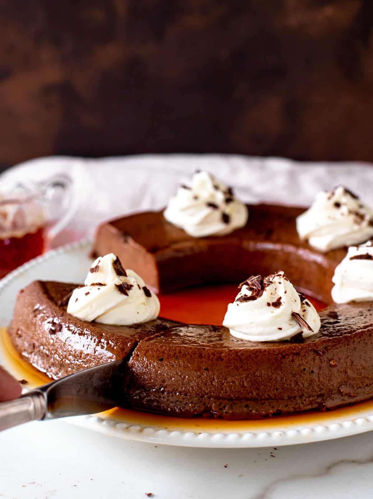Cutting a chocolate flan with dollops of cream, brown white background