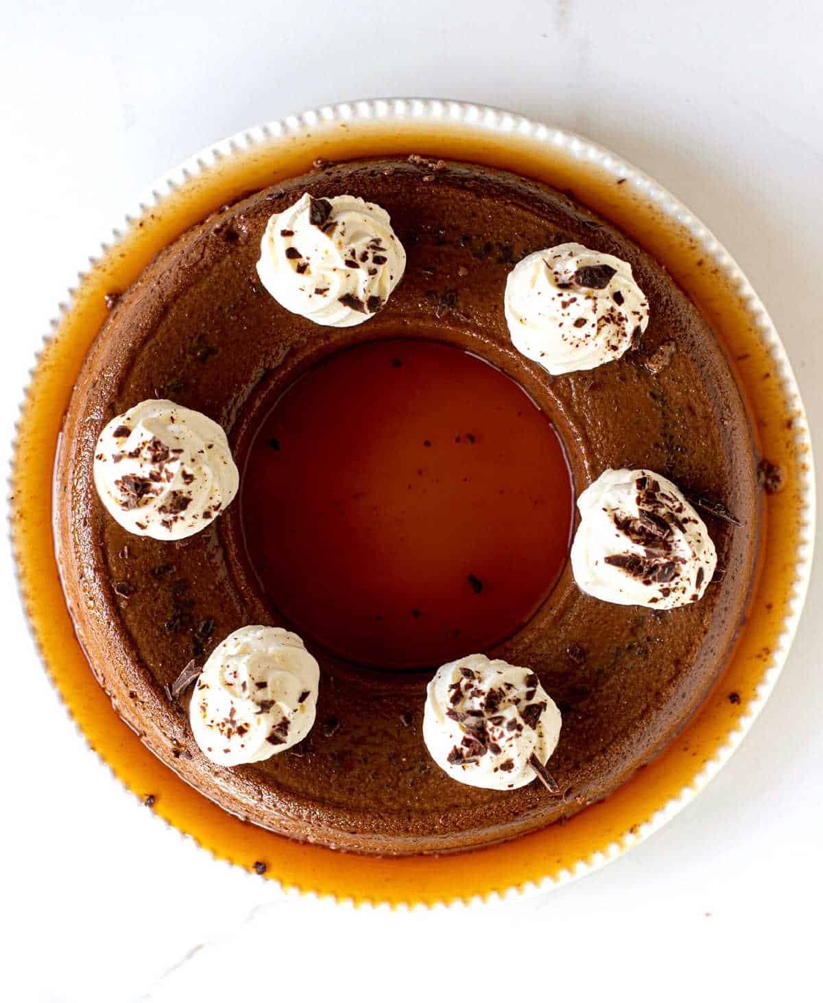 Top view of round chocolate flan with whipped cream dollops on white surface