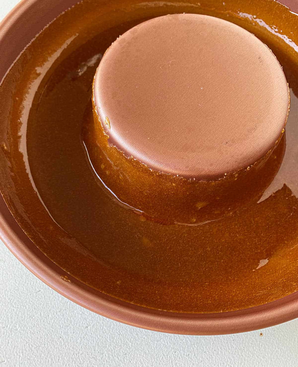 Partial view of copper flan pan coated with caramel on white surface