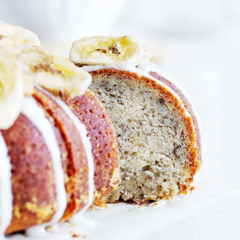 A slice of glazed banana bundt cake being pulled from the cake. Close up image with white background.