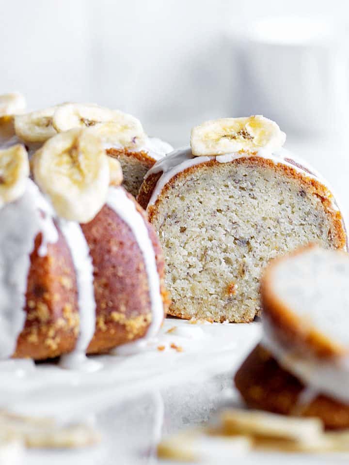Close up of glazed banana cake with some cut slices. White surface and background.