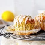 Wire rack with glazed lemon muffin in an open paper cup, white background.