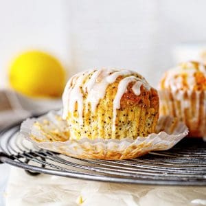 Wire rack with glazed lemon muffin in an open paper cup, white background.