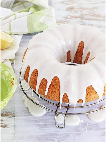 Glazed bundt cake on wire rack on white table, green props