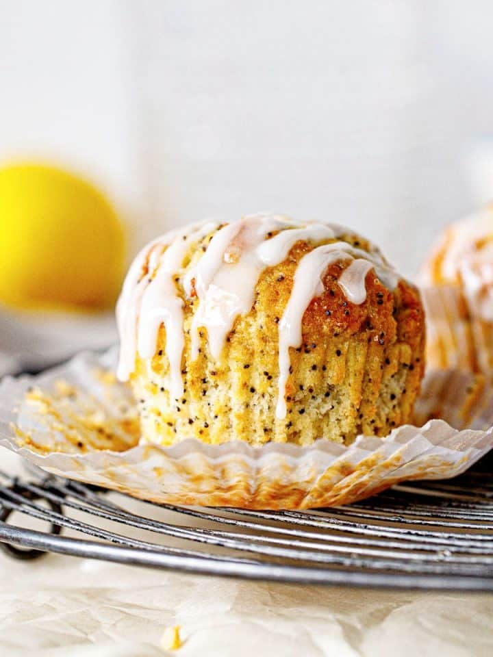 Wire rack with glazed lemon muffin in an open paper cup, white background