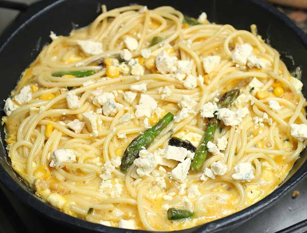 Cheese, asparagus, and parsley topped pasta frittata mixture in a dark skillet before baking.