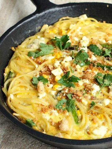 Close up of baked pasta frittata with parsley in a cast iron skillet on a beige surface.