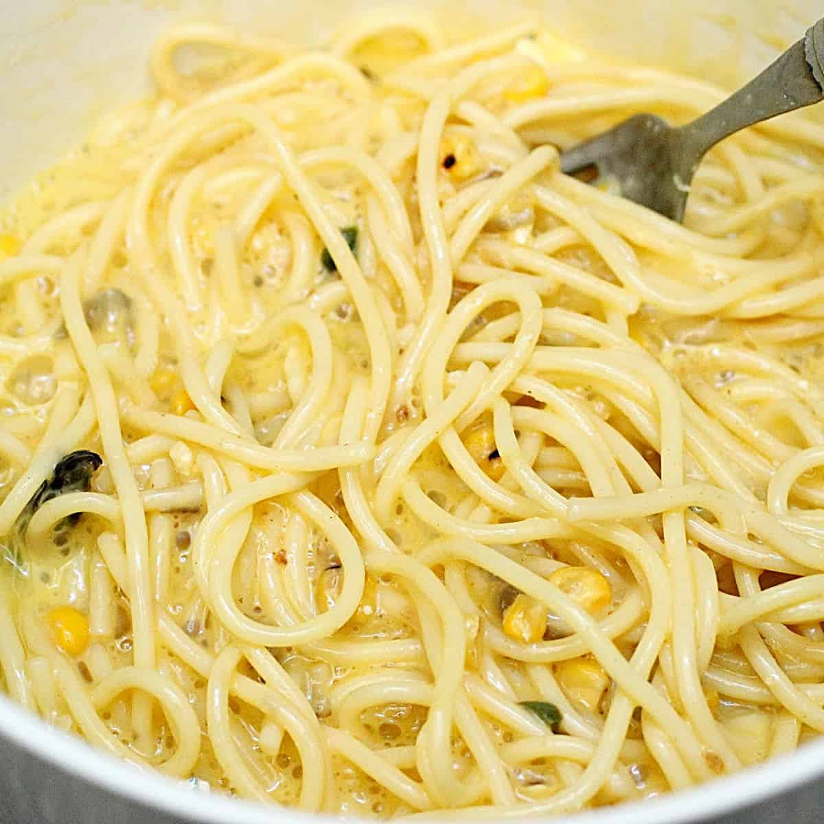 Mixing spaghetti with eggs in a bowl with a fork. Close up image.