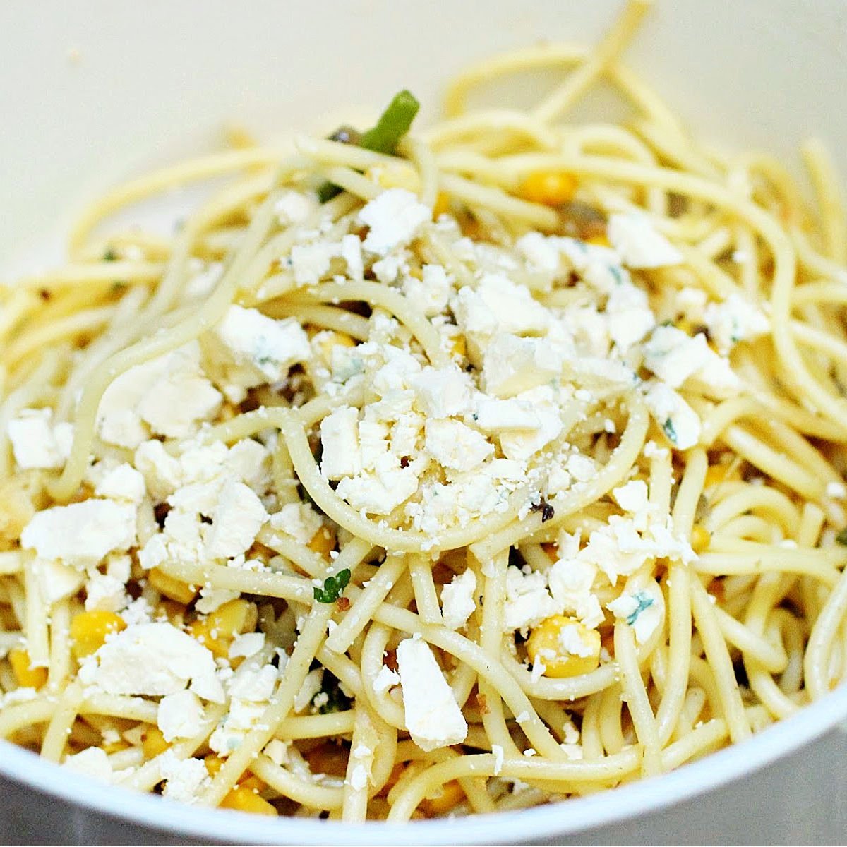 Feta cheese added to spaghetti in a white bowl.