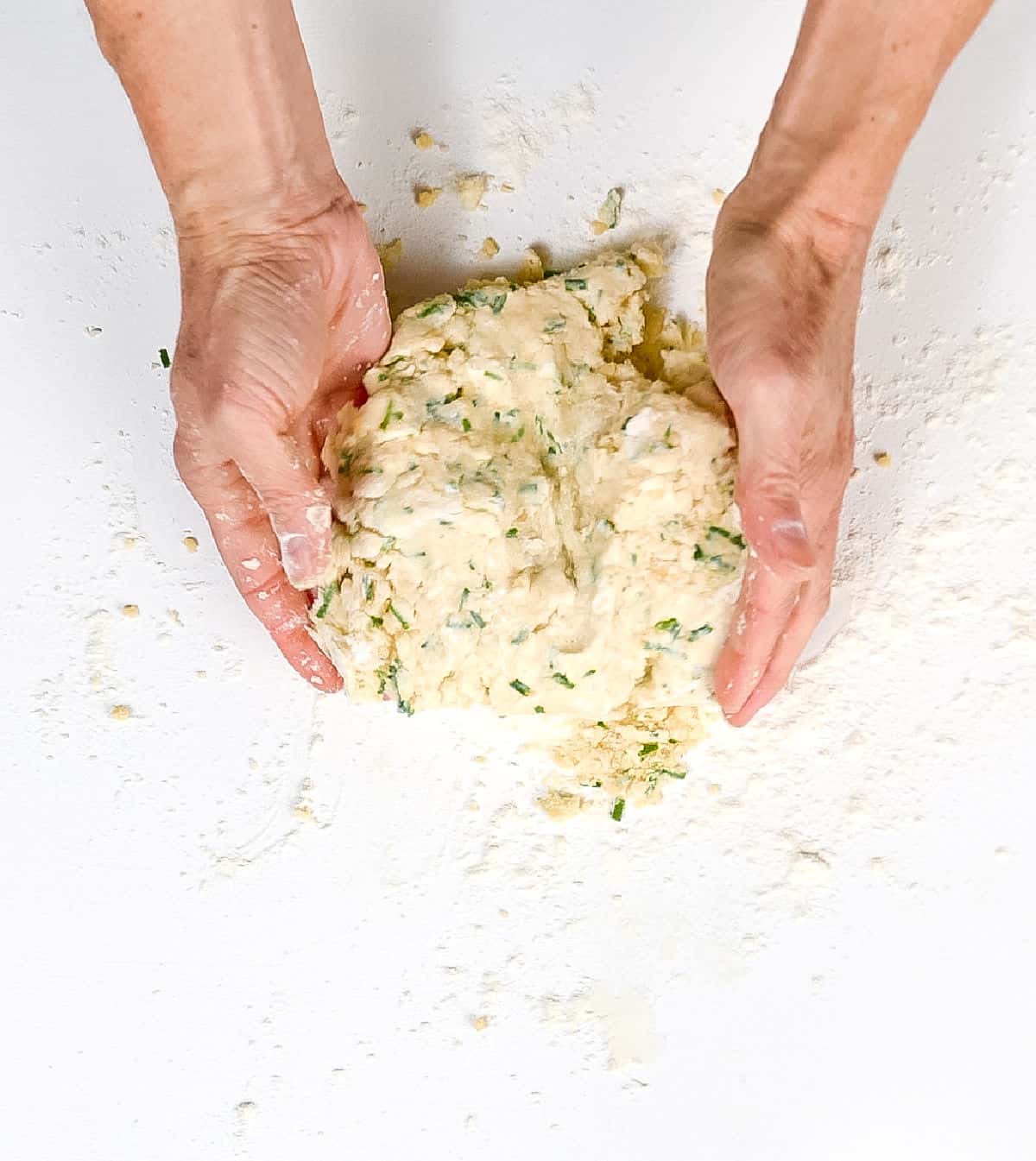 Gathering chive scone dough on a white surface.