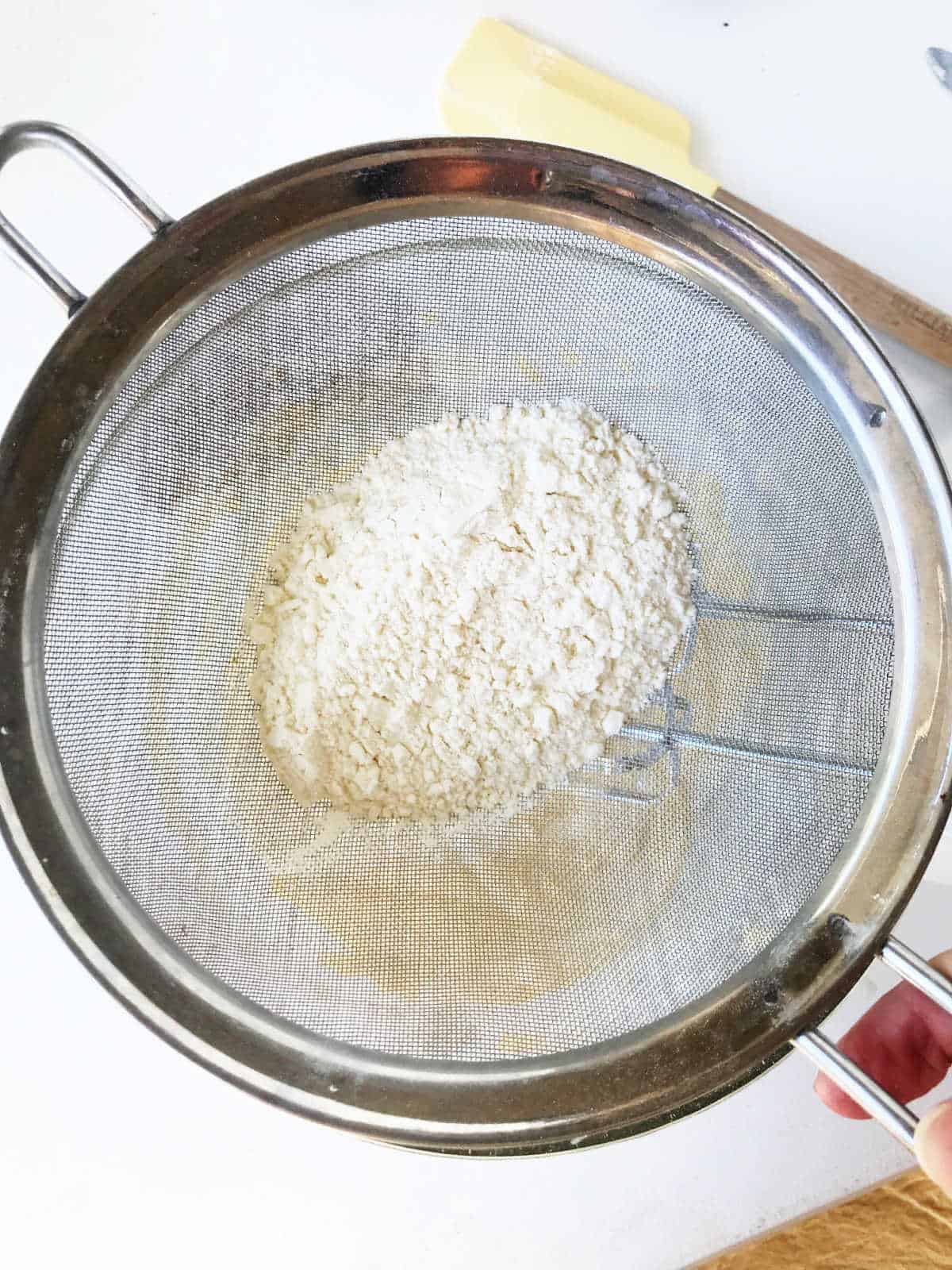 Sifter with flour mixture seen from above. White surface below.