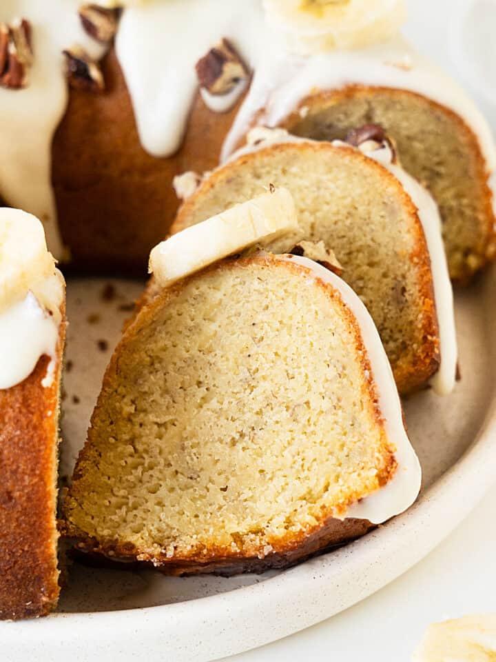 Close up of glazed banana bundt cake, some is sliced on a white plate.