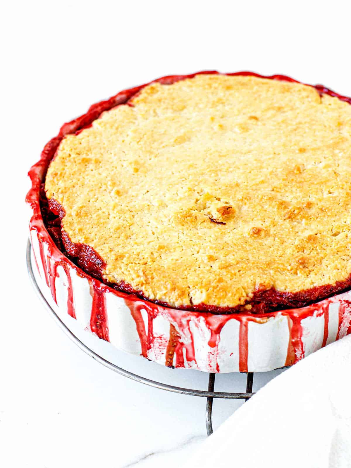 Partial view of round white dish with baked strawberry cobbler on white surface
