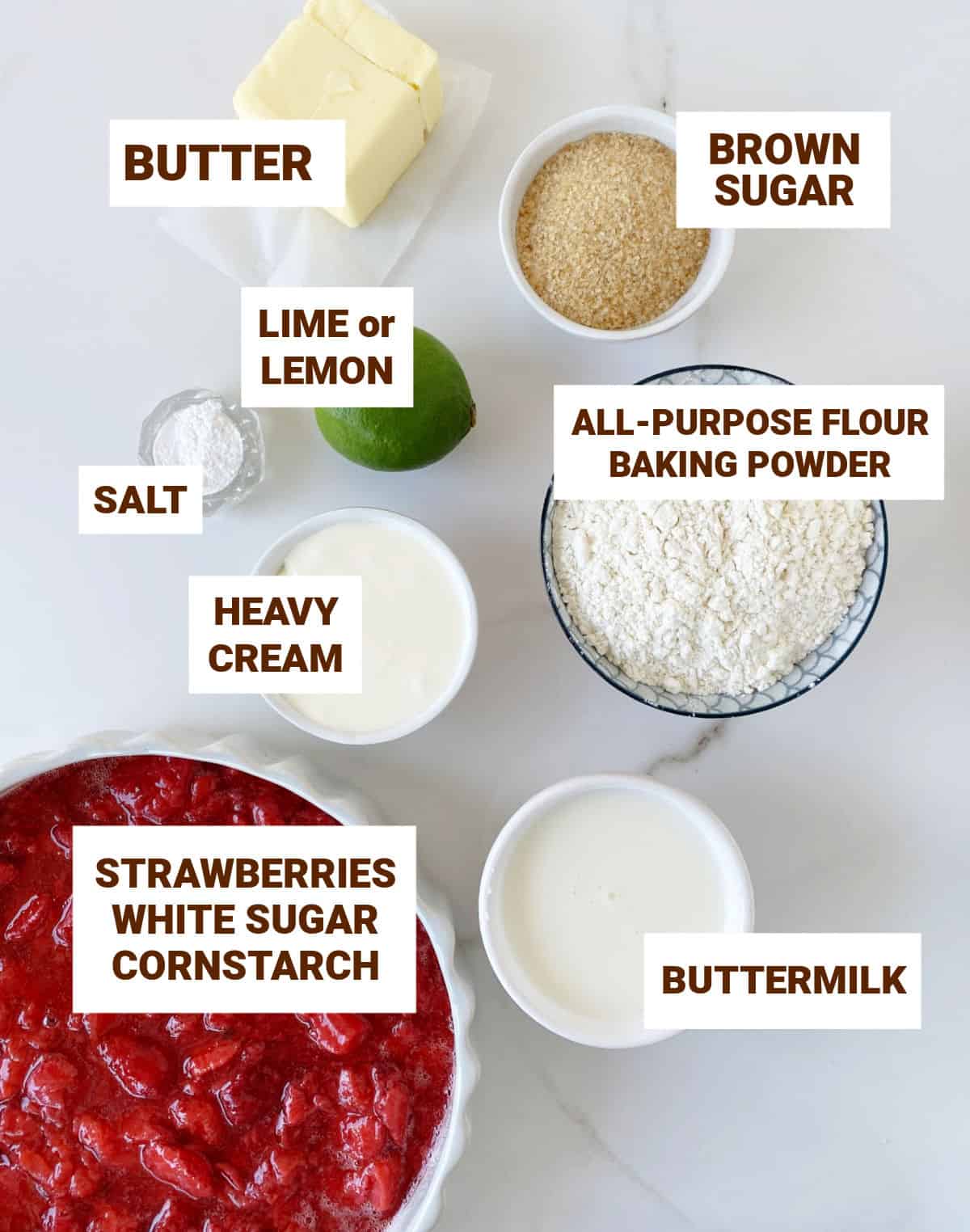 Greyish surface with ingredients in bowls strawberry cobbler including lime, butter, brown sugar, buttermilk, cream