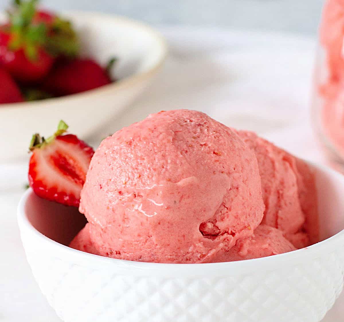 Close up of White patterned bowl with strawberry ice cream, more strawberries as background.