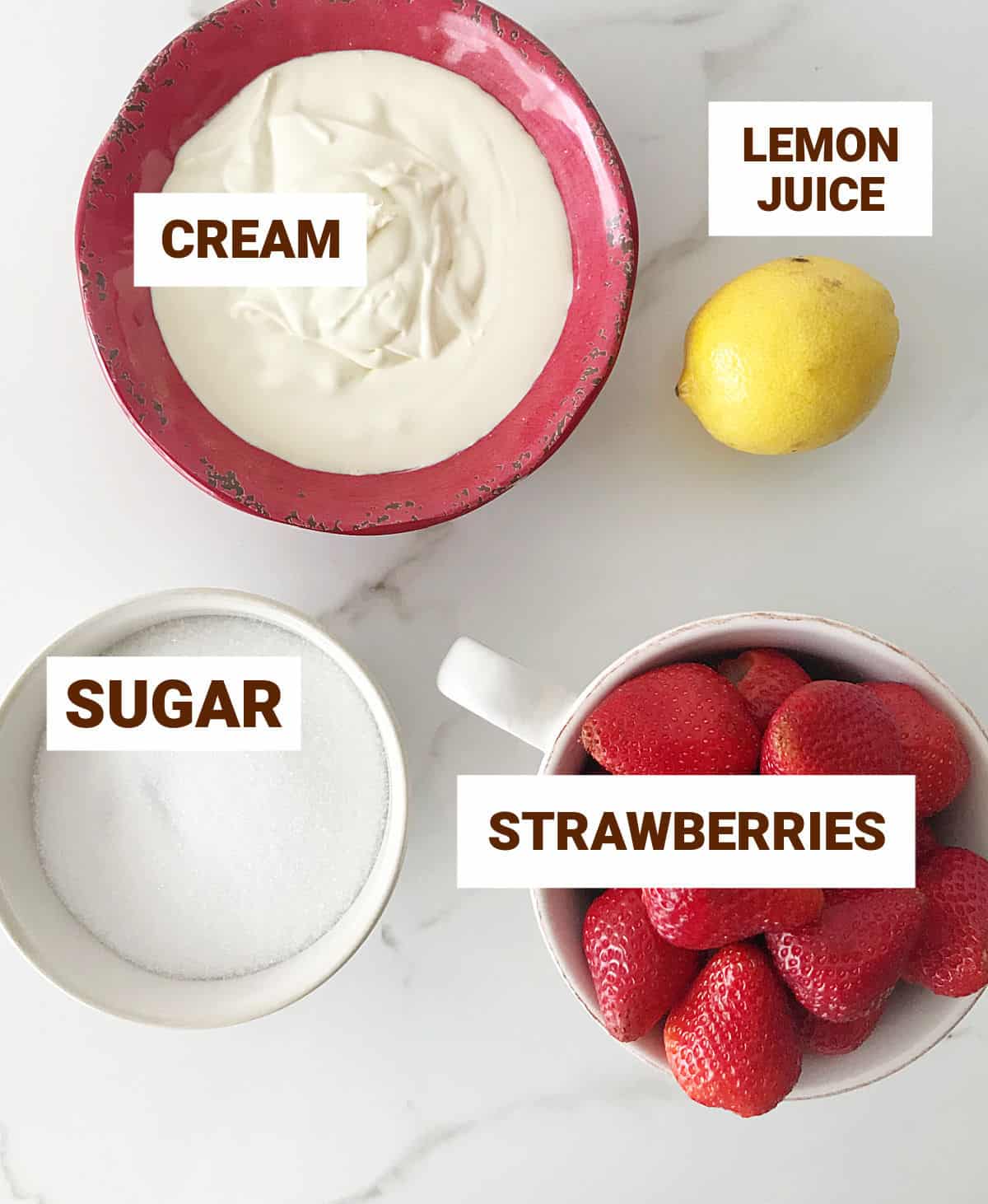 Ingredients for fresh strawberry ice cream on white surface, including lemon, cream, and sugar.