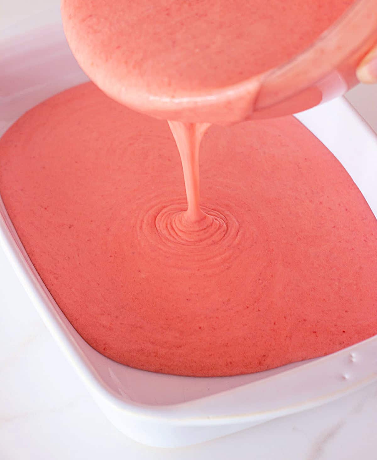 Pouring strawberry ice cream onto white ceramic shallow dish.