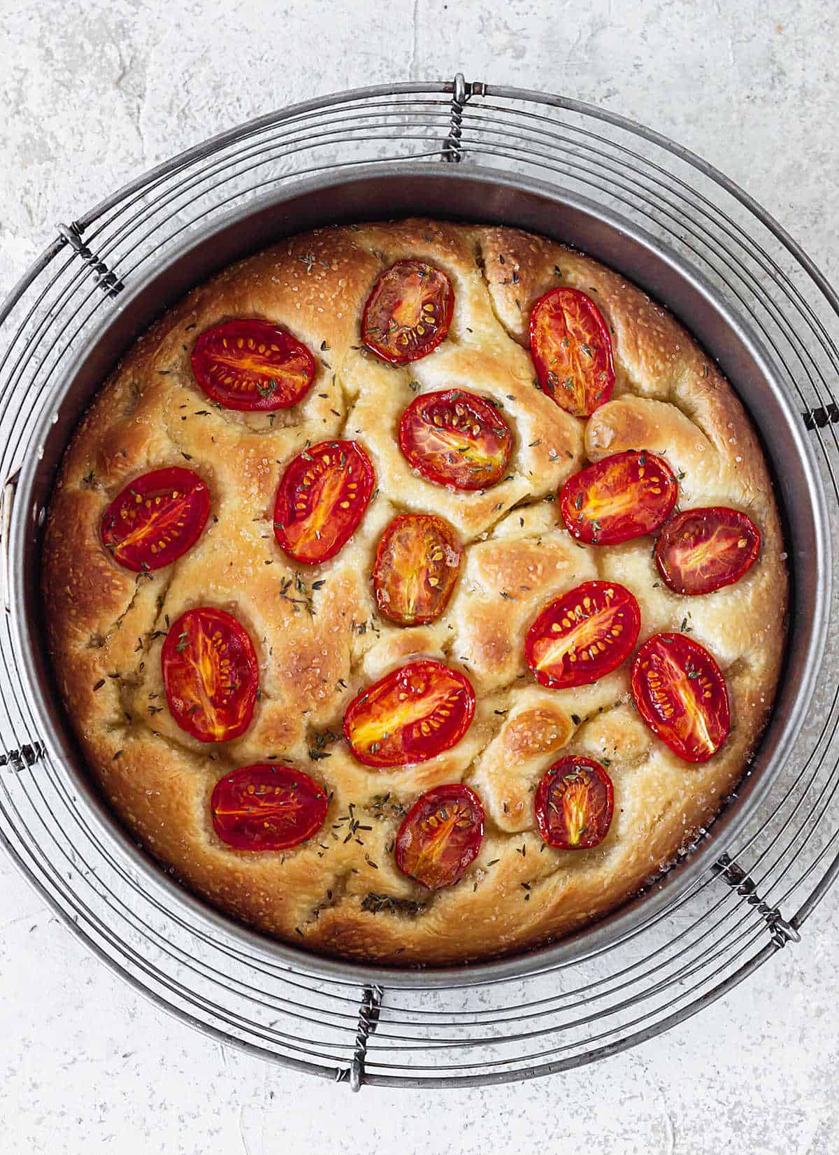 Top view of baked tomato focaccia on round pan on wire rack, grey surface