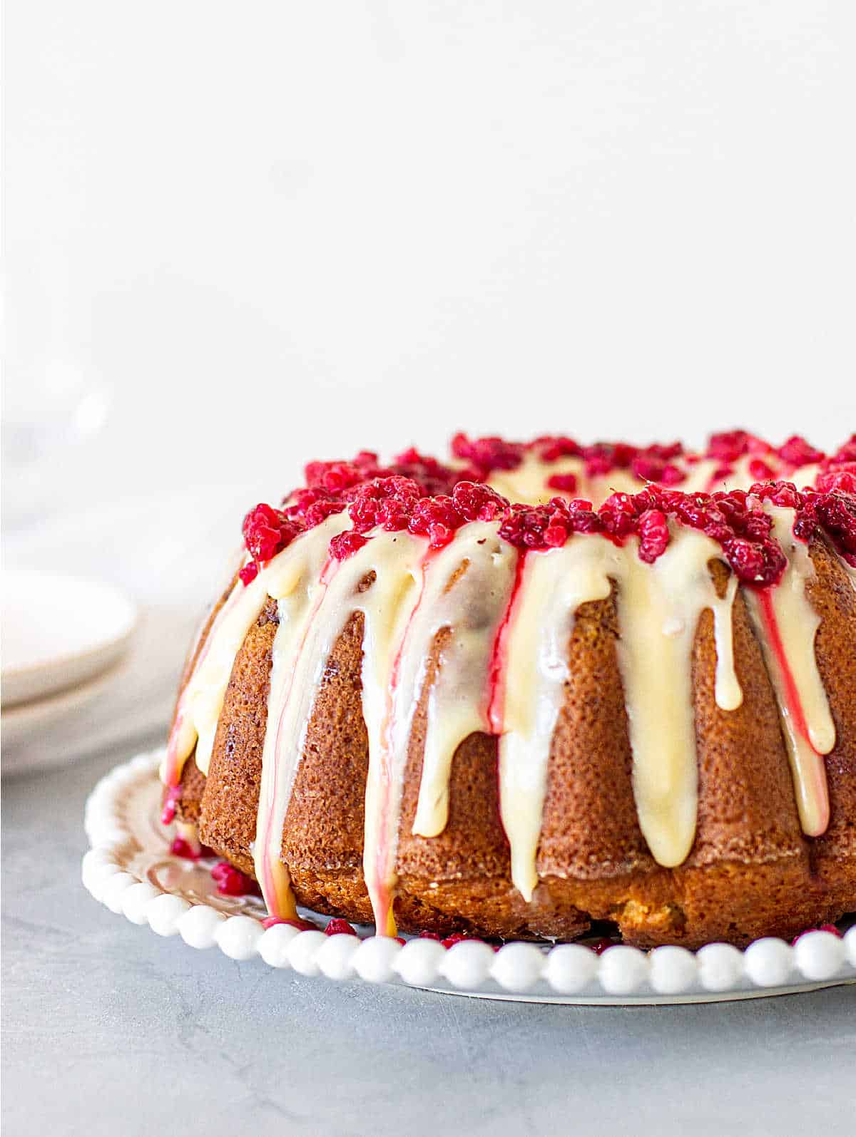 Partial view of white chocolate raspberry bundt cake on white plate, grey background