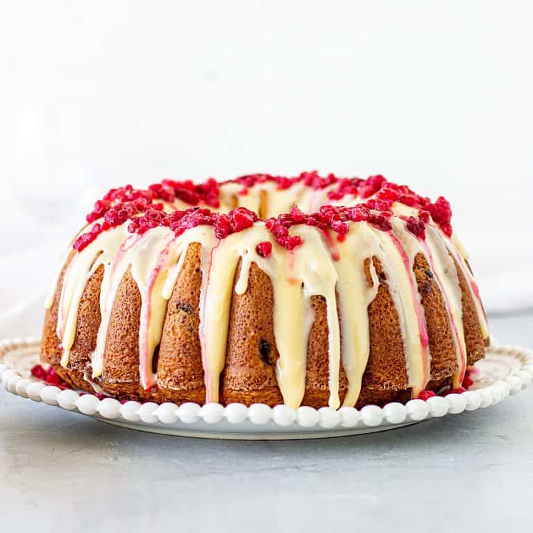 Front view of whole bundt with white chocolate and raspberries, white and grey background
