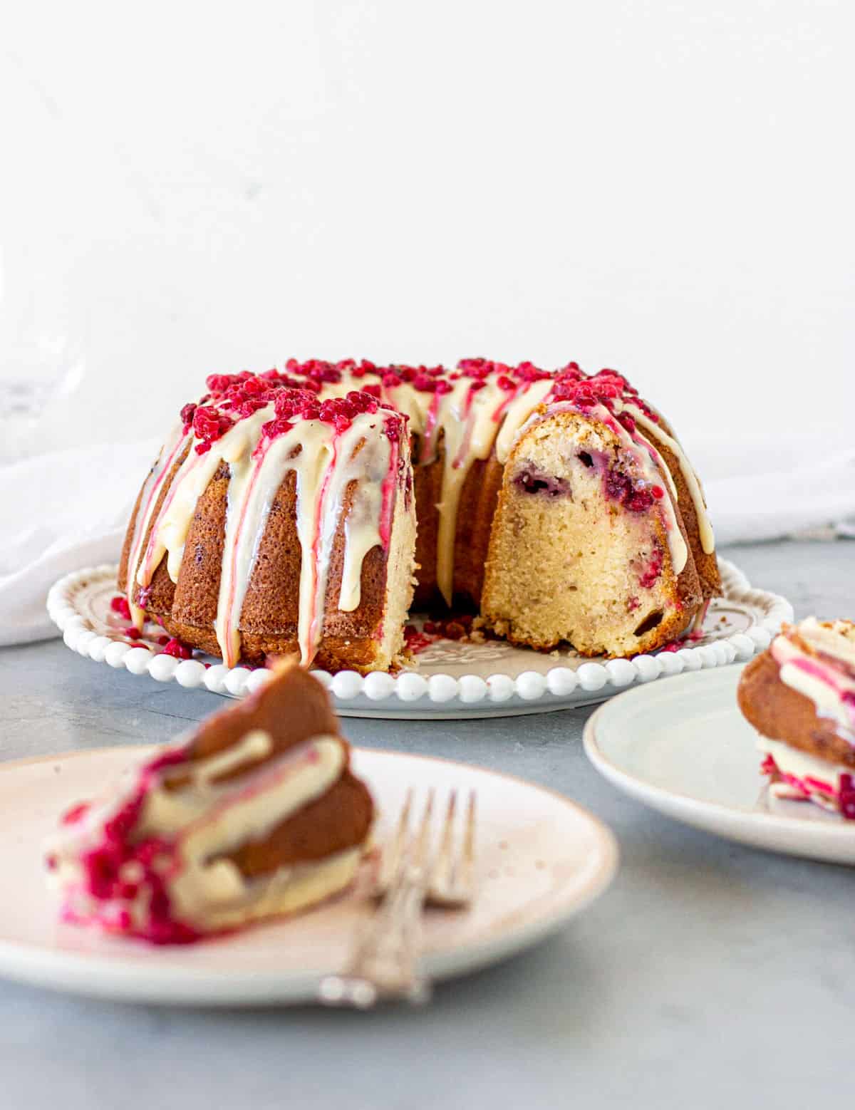White chocolate raspberry bundt cake on white plate, slice on another plate, grey background