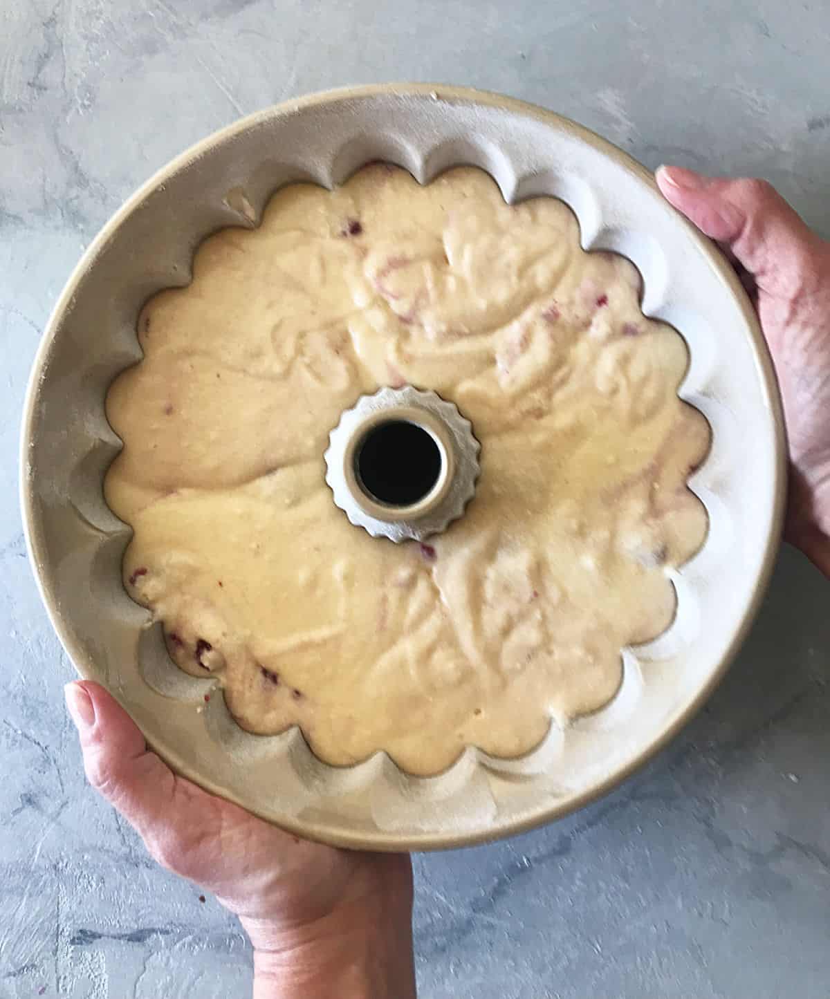 Hands holding cake pan with unbaked batter on marble surface