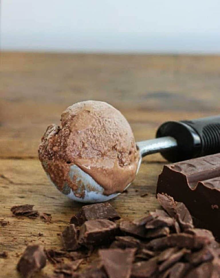 Scoop of chocolate ice cream on a wooden table, chopped chocolate around