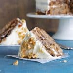 Blue surface with slice of hummingbird cake, more in brown background on cake stand