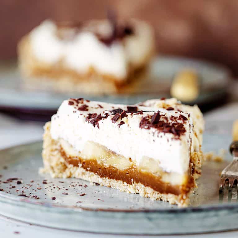 Close up slice of banoffee pie on grey plate, another serving in background