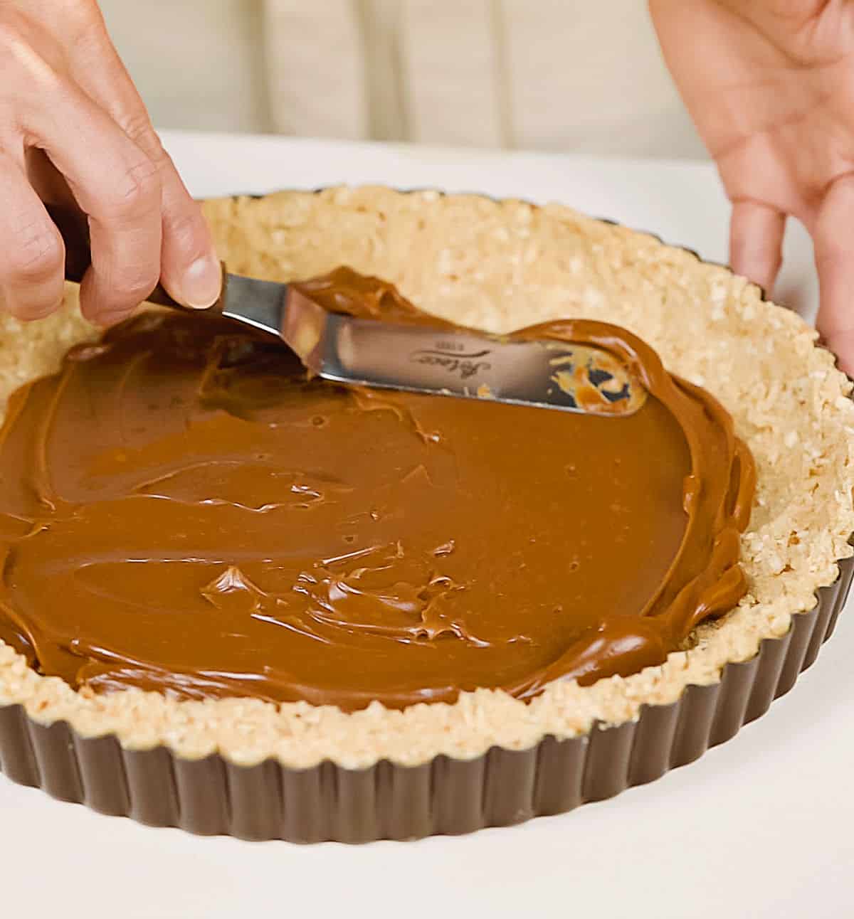 Spreading dulce de leche on cookie crust on white table