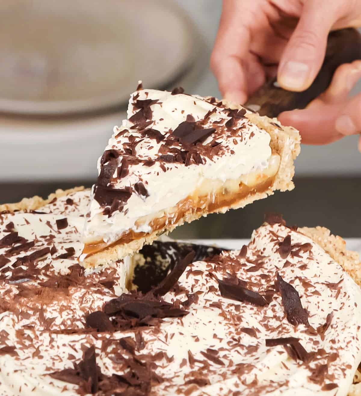 Lifting slice of banoffee pie from whole pie with cake server.