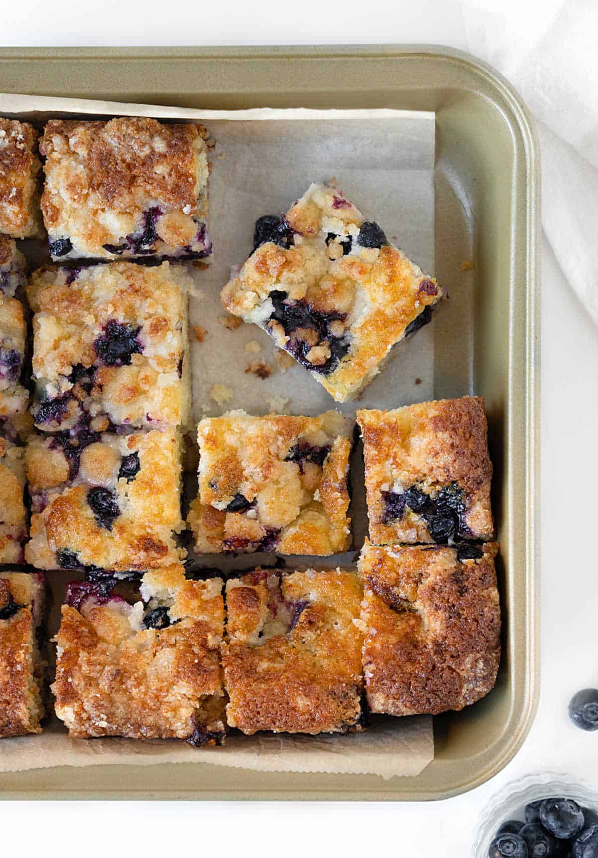 Squares of blueberry crumb cake in a metal square pan with parchment paper.