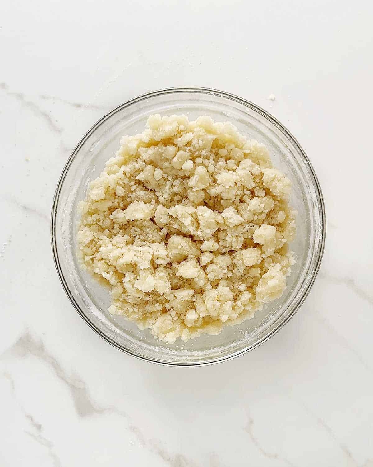 Crumble mixture in a glass bowl on a white marble surface.