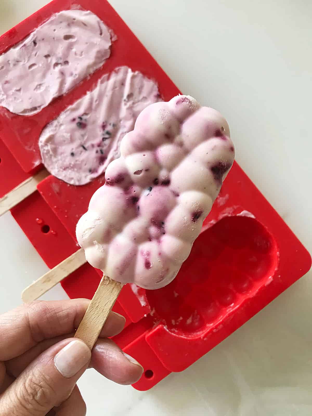 Hand holding frozen popsicle: red mold below with more 