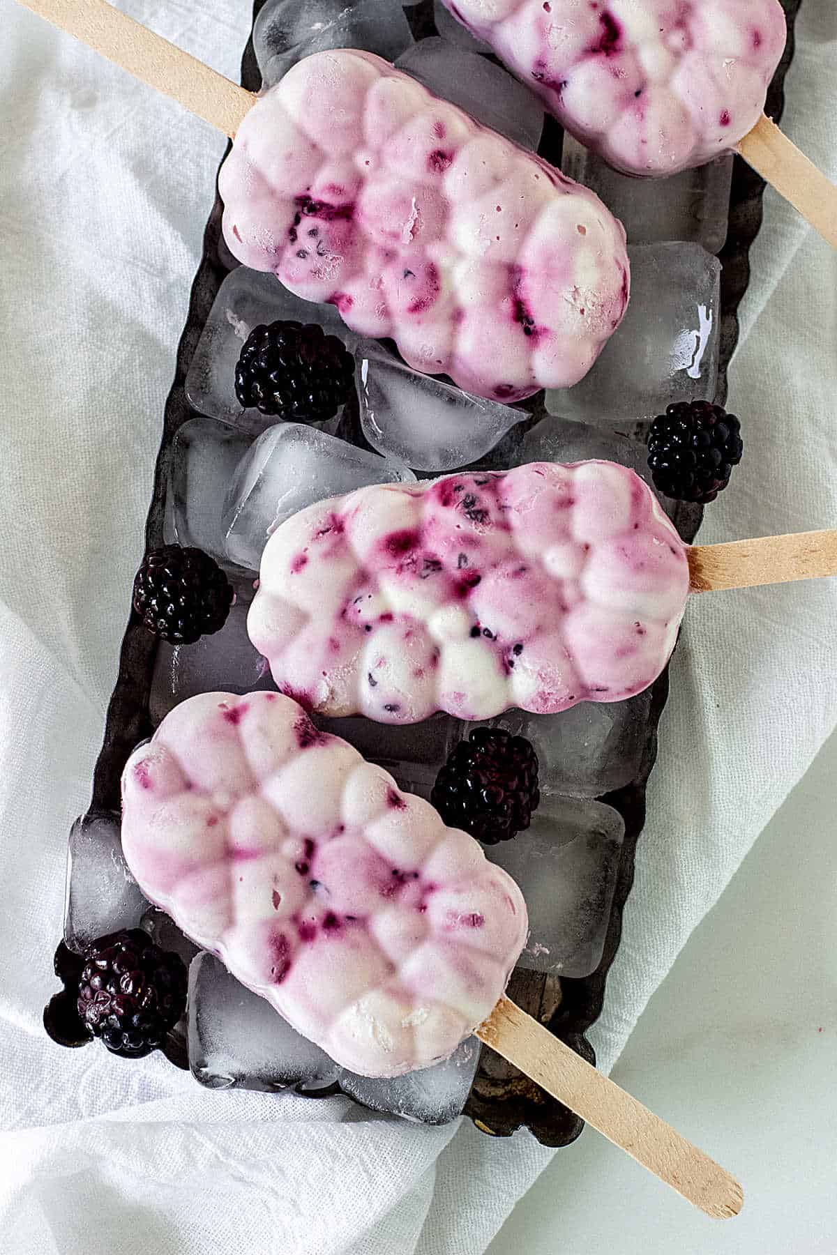 Top view of bubble shaped berry ice cream popsicles on a metal surface with ice cubes.