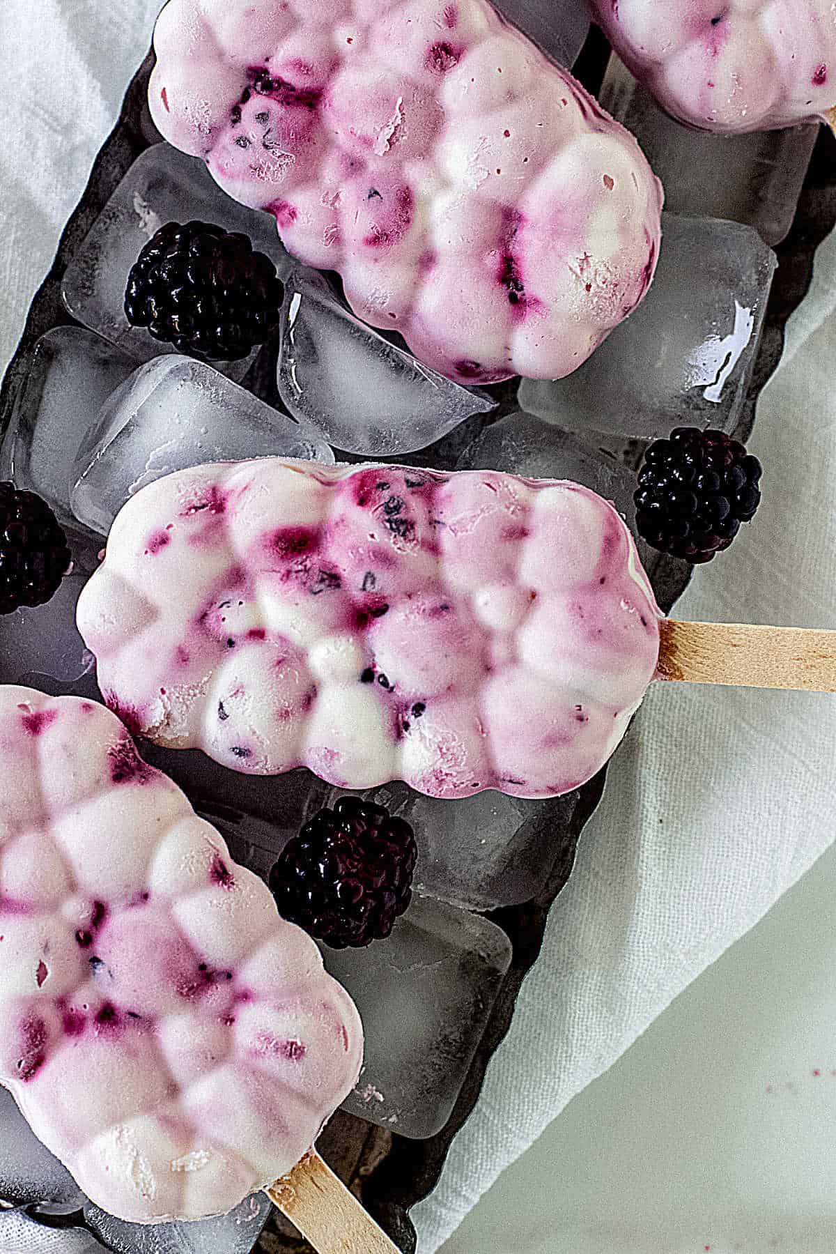 Overview of several bubble shaped berry ice cream popsicles on ice cubes in metal pan
