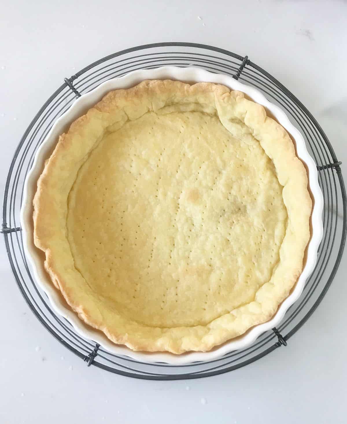 Baked pie crust on wire rack on white surface