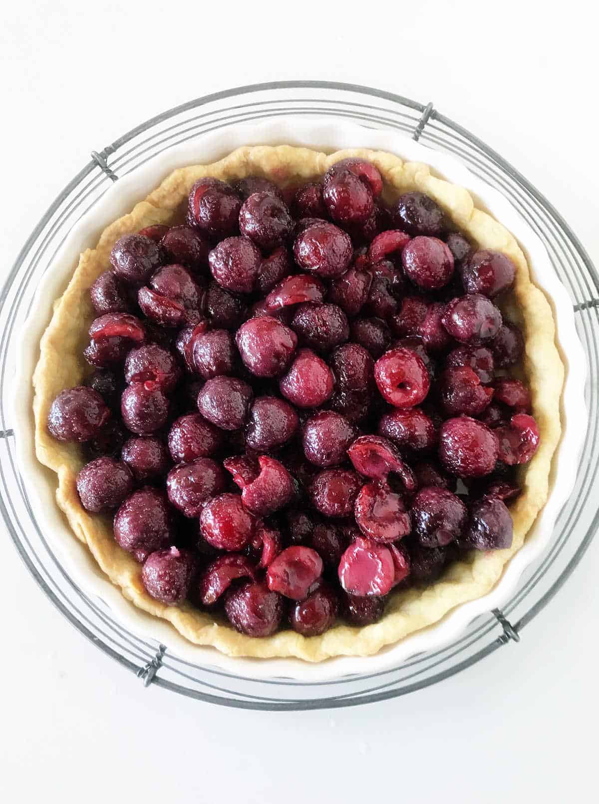 Cherry filled pie crust on wire rack, white background