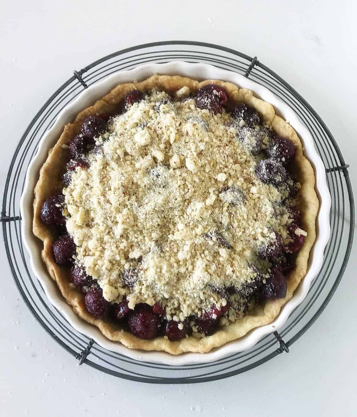 Over view of unbaked cherry crumb pie on wire rack on white surface