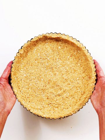 White surface with hands holding a graham cracker pie pan. Top view.