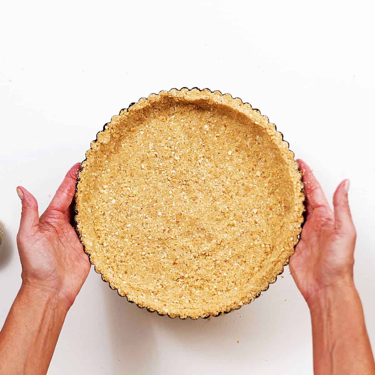 Holding graham cracker crust with both hands on white surface.