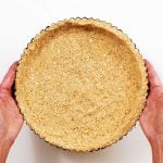 Holding a round graham cracker crust on a white surface. Top view.