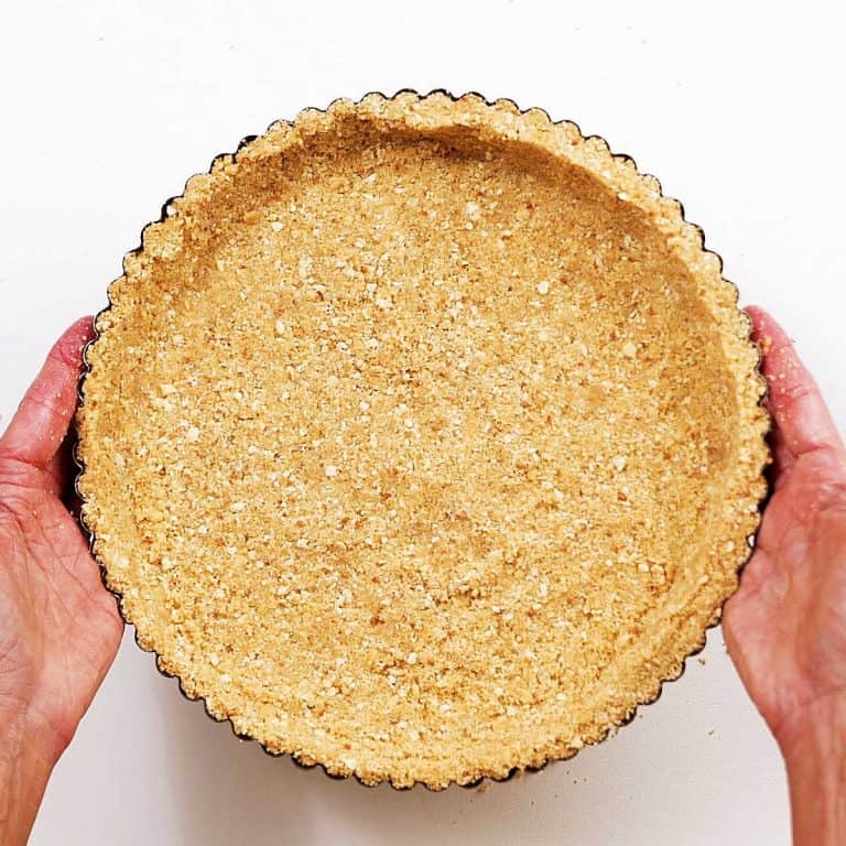 Hands holding round graham cracker crust on a white surface