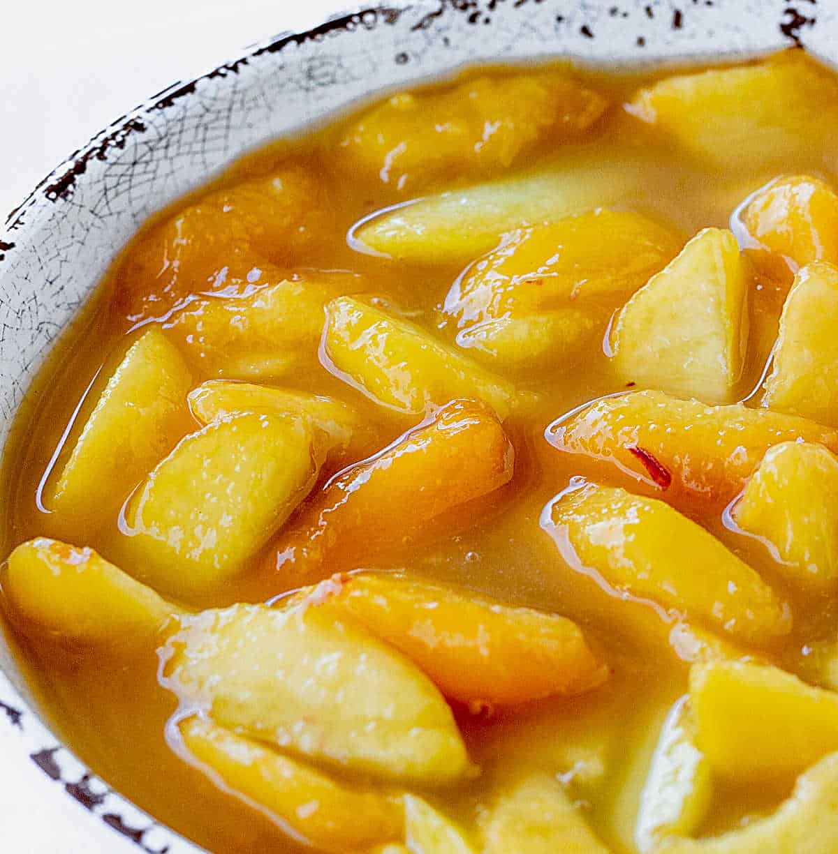 Close up image of homemade peach filling in a white and brown rim bowl.