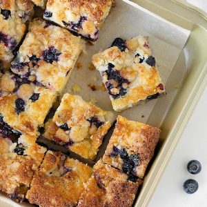 Close up top view of squares of blueberry crumb cake in a metal square pan with parchment paper.